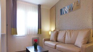A living room with a beige sofa, a small table with a vase of flowers, and a radiator. - Charming Apartment for Five Guests (Port-Bail-sur-Mer)