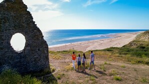 A stone ruin with a circular opening, overlooking a beach with people walking. - Charming Apartment for Five Guests (Port-Bail-sur-Mer)