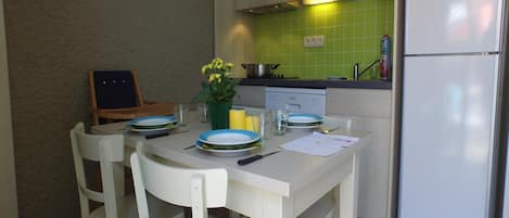 Cocina compacta con armarios blancos, microondas, refrigerador y una mesa de comedor lista para cuatro personas con sillas.