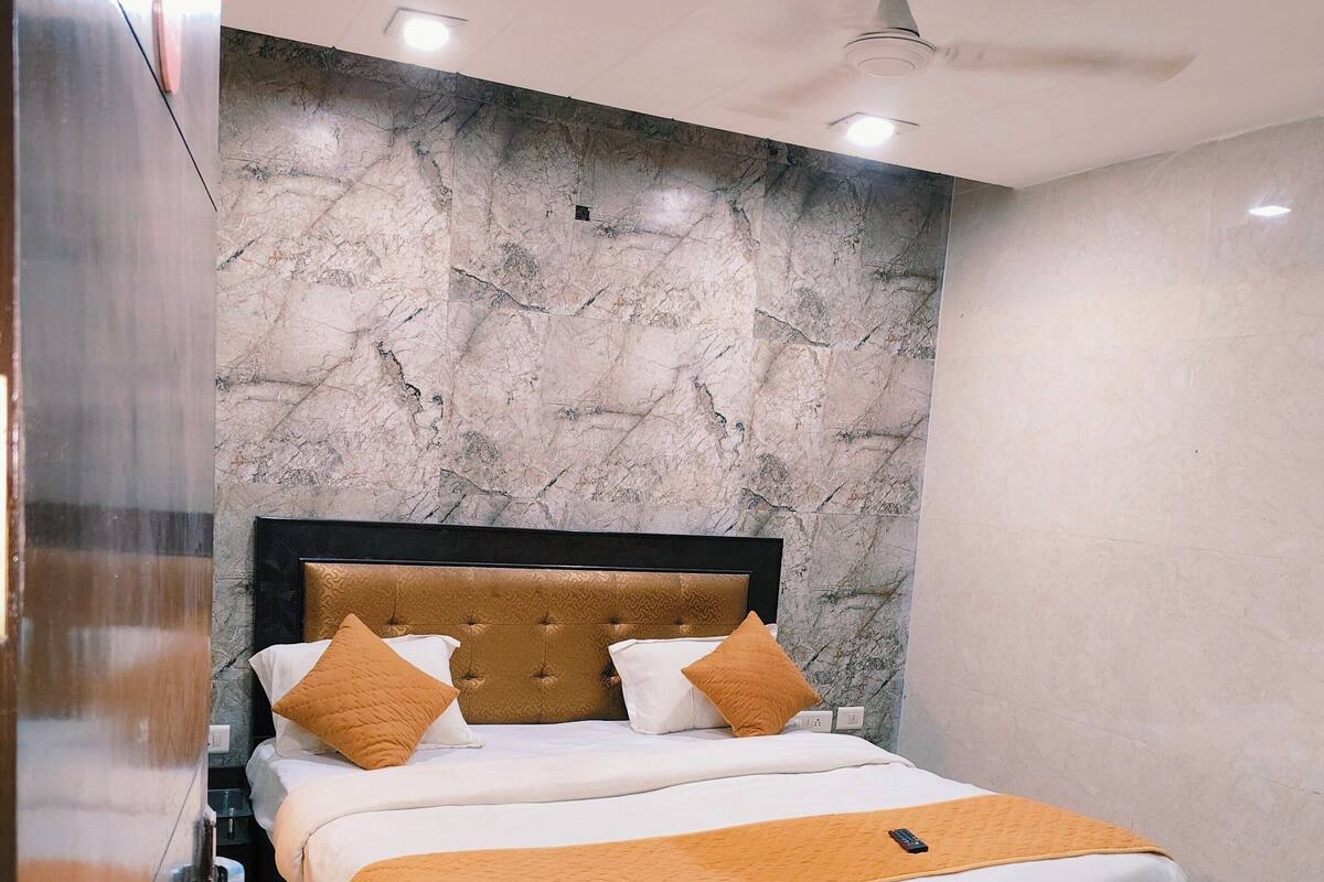 A modern bedroom with a marble headboard, a bed with white and orange bedding, and a ceiling fan.