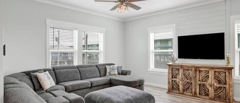 A modern living room with a sectional sofa, a wooden cabinet, and a ceiling fan.