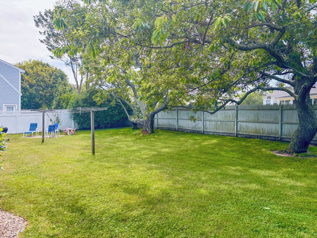 A backyard with a wooden fence, a tree, and a patio area with chairs.