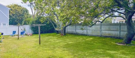 A backyard with a wooden fence, a tree, and a patio area with chairs.