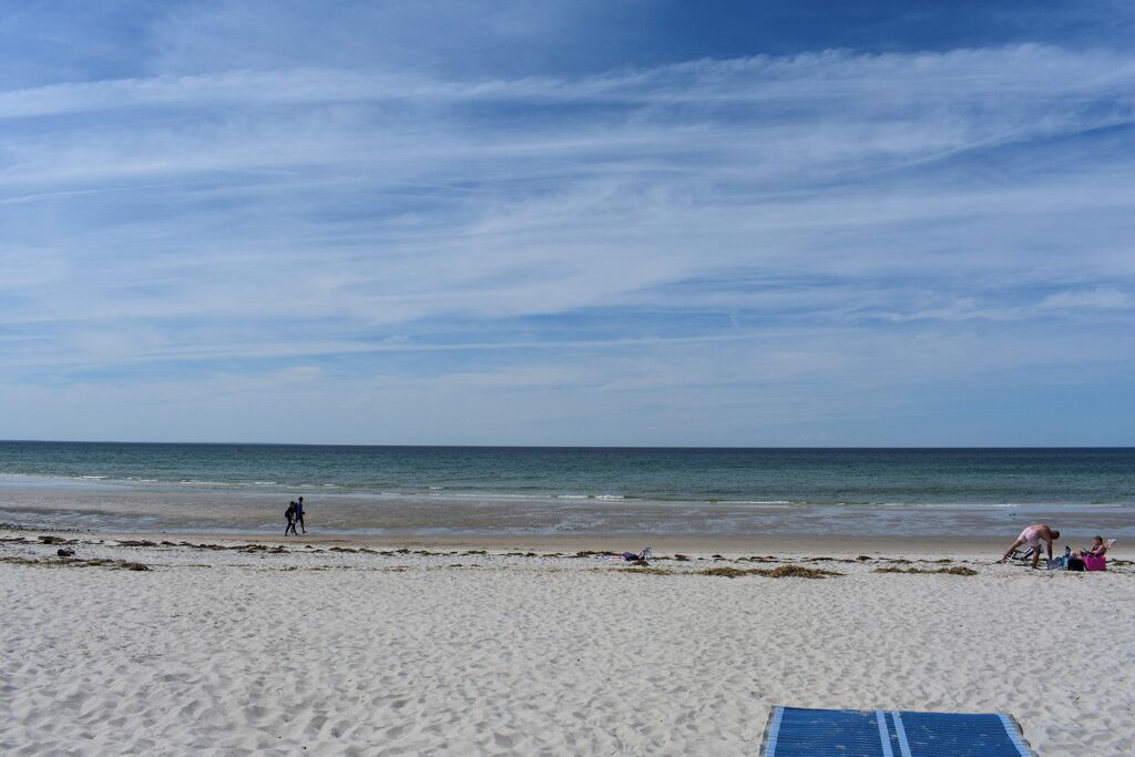 Ein sandiger Strand mit einigen Personen und einer blauen Liege.