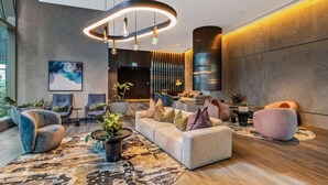Un hall d’entrée moderne, doté d’un ensemble de canapés, de fauteuils, d’une table basse et d’un luminaire circulaire original.