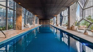 Une piscine intérieure de forme longue et étroite, entourée de grandes fenêtres et agrémentée d’espaces de détente modernes.