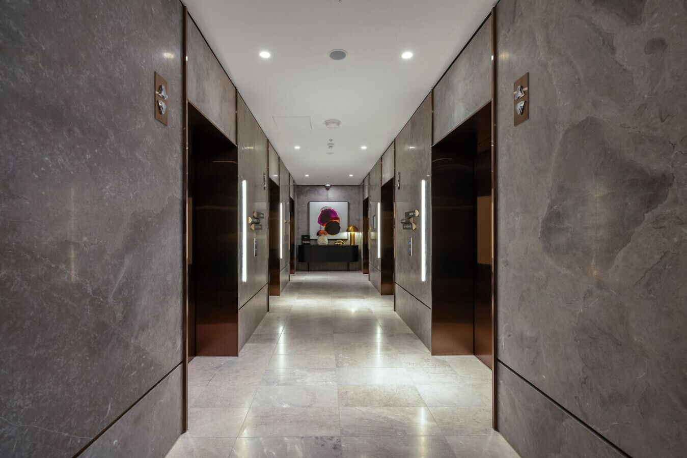 A hallway with marble walls and floors, leading to a reception area with a counter and a large abstract painting.
