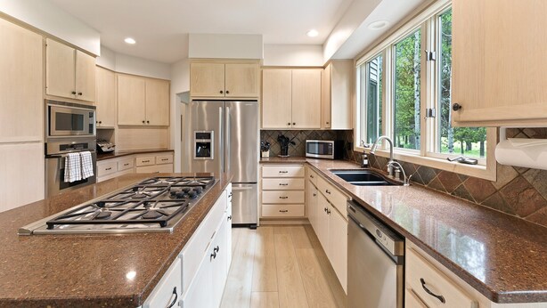 Una cocina moderna con una isla central, electrodomésticos de acero inoxidable y un amplio ventanal que proporciona luz natural.