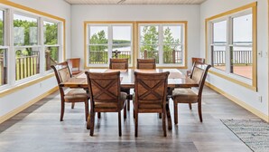 A spacious dining area with a large table and chairs, large windows with a view of a lake, and a ceiling fan. - 4BR Lakefront Fishing, Dogs OK Devils Lake (Crary)