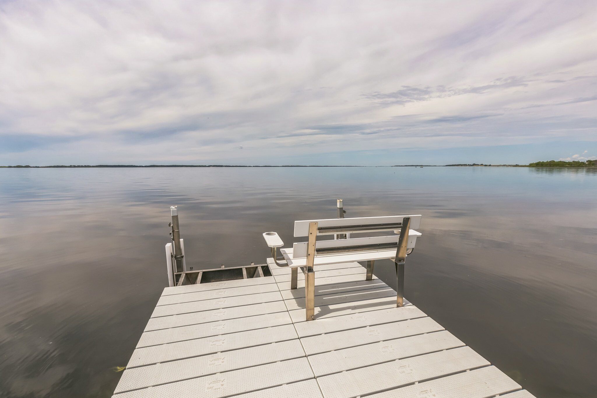 A wooden pier extending into calm water with a bench and a small table.