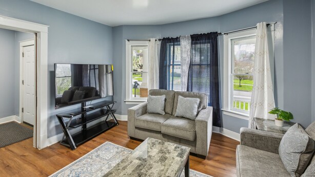 A living room with a sofa, a coffee table, a TV, and a window with curtains. - Comfy 3br Flat Close To The Falls 3 Bedroom Apts (Niagara Falls)
