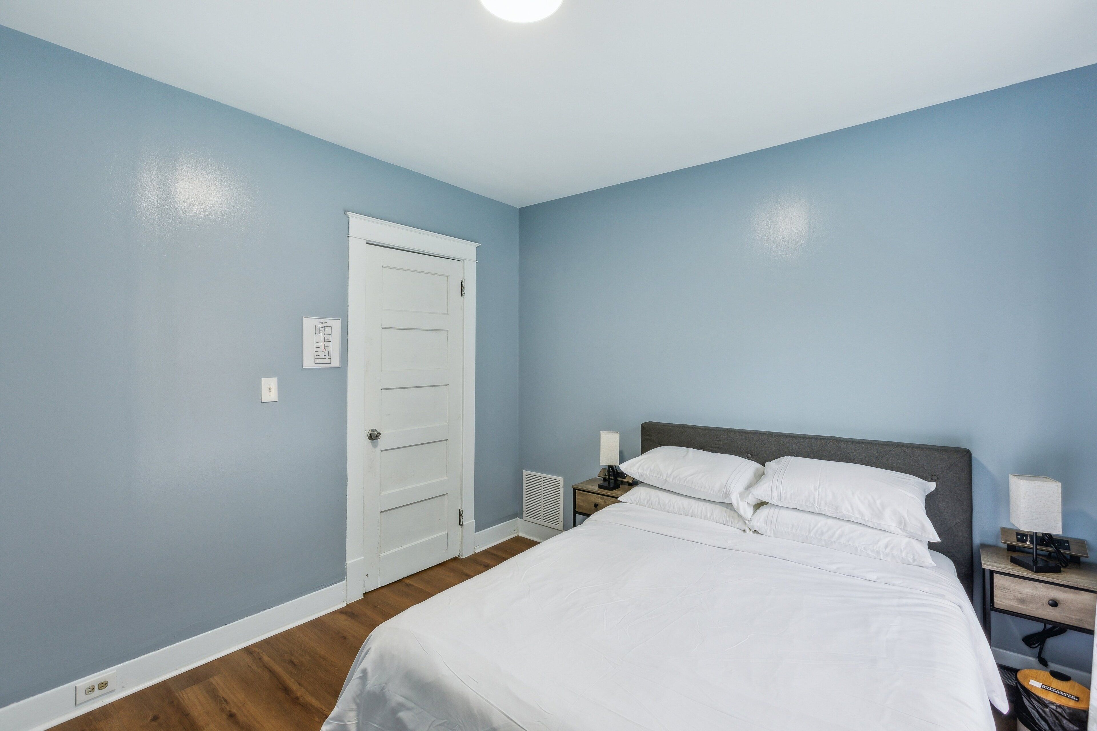 Ein Schlafzimmer mit einem Bett, einem Nachttisch, einer Lampe und einer weißen Tür.