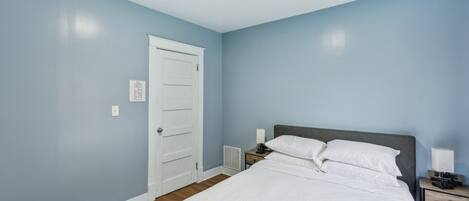 A bedroom with a bed, nightstand, lamp, and a white door.