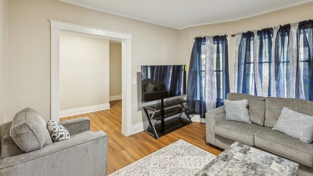 A living room with a grey sofa, a TV on a stand, and a patterned rug. - Cozy Upper Flat Minutes From Niagara Falls 3 Bedroom Apts (Niagara Falls)