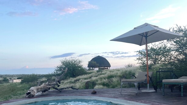 Une piscine avec un espace détente, un grand parasol et une vue sur une montagne en arrière-plan.