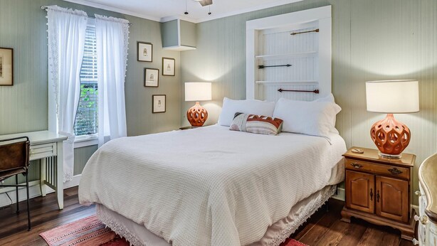 Un dormitorio ordenado con cama, mesitas de noche, un escritorio y ventilador de techo.