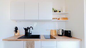 Una cocina moderna con armarios blancos, encimera de madera, un lavamanos, una tetera y una cafetera.