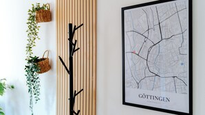 Un mapa enmarcado de Göttingen en una pared, una pieza decorativa de metal negro y dos cestas de mimbre con plantas.
