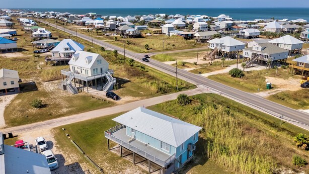 Vista aérea de una zona residencial costera con casas, una carretera y una playa al fondo.