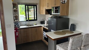 Una cocina compacta con gabinetes de madera, un lavamanos de acero inoxidable, un microondas integrado, un refrigerador y una cafetera.