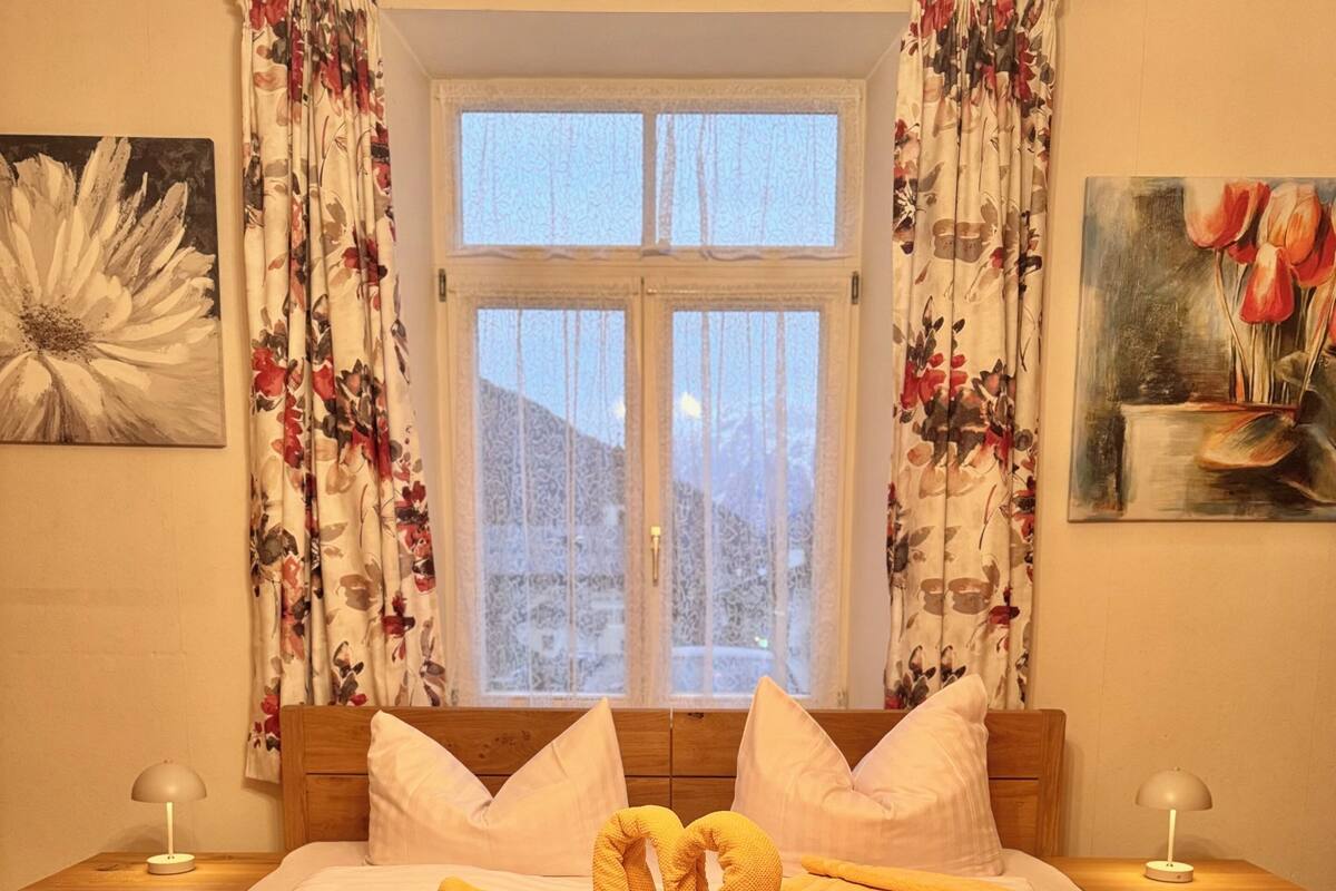 A double bed with a floral curtain and a painting of tulips on the wall.