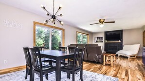 A modern living room with a dining area, wooden flooring, a ceiling fan, and a fireplace.