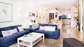 Un salon moderne avec un canapé bleu, une table basse blanche et un coin cuisine à l’arrière-plan.