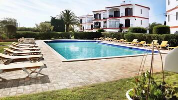 A swimming pool with lounge chairs, surrounded by a paved area and greenery.