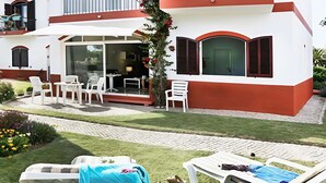 Un bâtiment moderne doté d’un patio avec des chaises blanches et une table, le tout entouré d’une pelouse et d’un jardin bien entretenus.