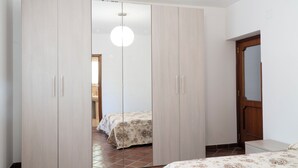 Ett sovrum med en stor garderob, en säng med blommigt sänglinne och en taklampa.