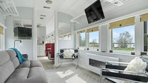 A modern interior with a sofa, a kitchen area, and large windows offering a view. - Crooked Lake Express (Alanson)