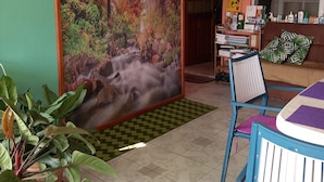 Ein Zimmer mit einer großen Wandmalerei von einer Waldszene, einem Deckenventilator, einem Bücherregal und einer Sitzecke mit Sofa und Sesseln.