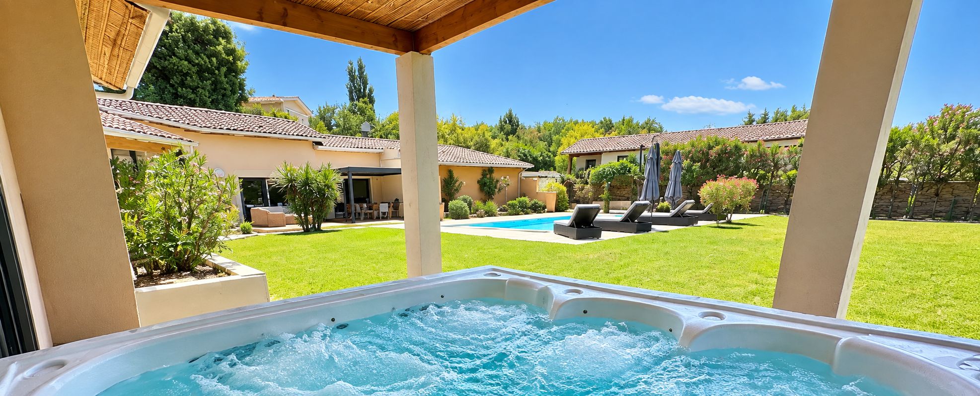 Un bain à remous avec vue sur un jardin, une piscine et une maison avec un toit en tuiles.