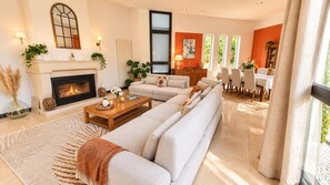 A modern living room with a fireplace, a sofa set, a dining area, and a view of greenery outside. - Magnificent villa with a pool and spa near Bordeaux (La Brède)