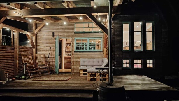A rustic wooden cabin with a loft bedroom, a cozy living area with a sofa, and a wooden deck. - Tiny House Design in a Vacation Park Near an Eco-Village (Steyerberg)