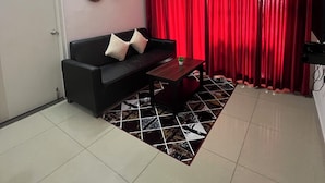 A living room with a black sofa, a small wooden table, red curtains, a ceiling fan, and a tiled floor. - 2-bedroom apartment in delightful Manipal with AC, WiFi, fitness room (Manipal)