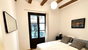 Una camera da letto con un letto, una finestra con tende, un quadro appeso al muro e travi a vista al soffitto.