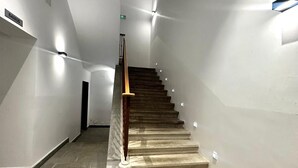 Una scala con ringhiera in legno e gradini in pietra, circondata da pareti bianche e un soffitto con illuminazione a incasso.