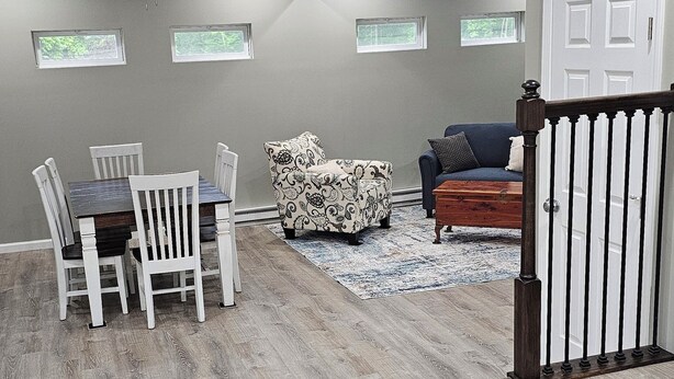 A spacious room with a dining table, chairs, a patterned sofa, and a wooden floor. - Charming 2-bedroom cottage in Beautiful Milford Center with WiFi, AC (Milford Center)