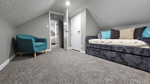 A bedroom with a sloped ceiling, a teal armchair, a dark patterned sofa, and a bed with multiple pillows. - Charming 2-bedroom cottage in Beautiful Milford Center with WiFi, AC (Milford Center)