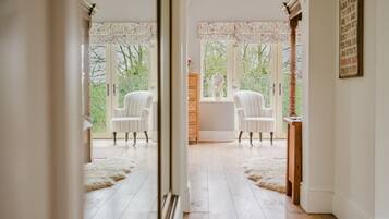 A room with two white upholstered chairs, a wooden cabinet, and a view through large windows.