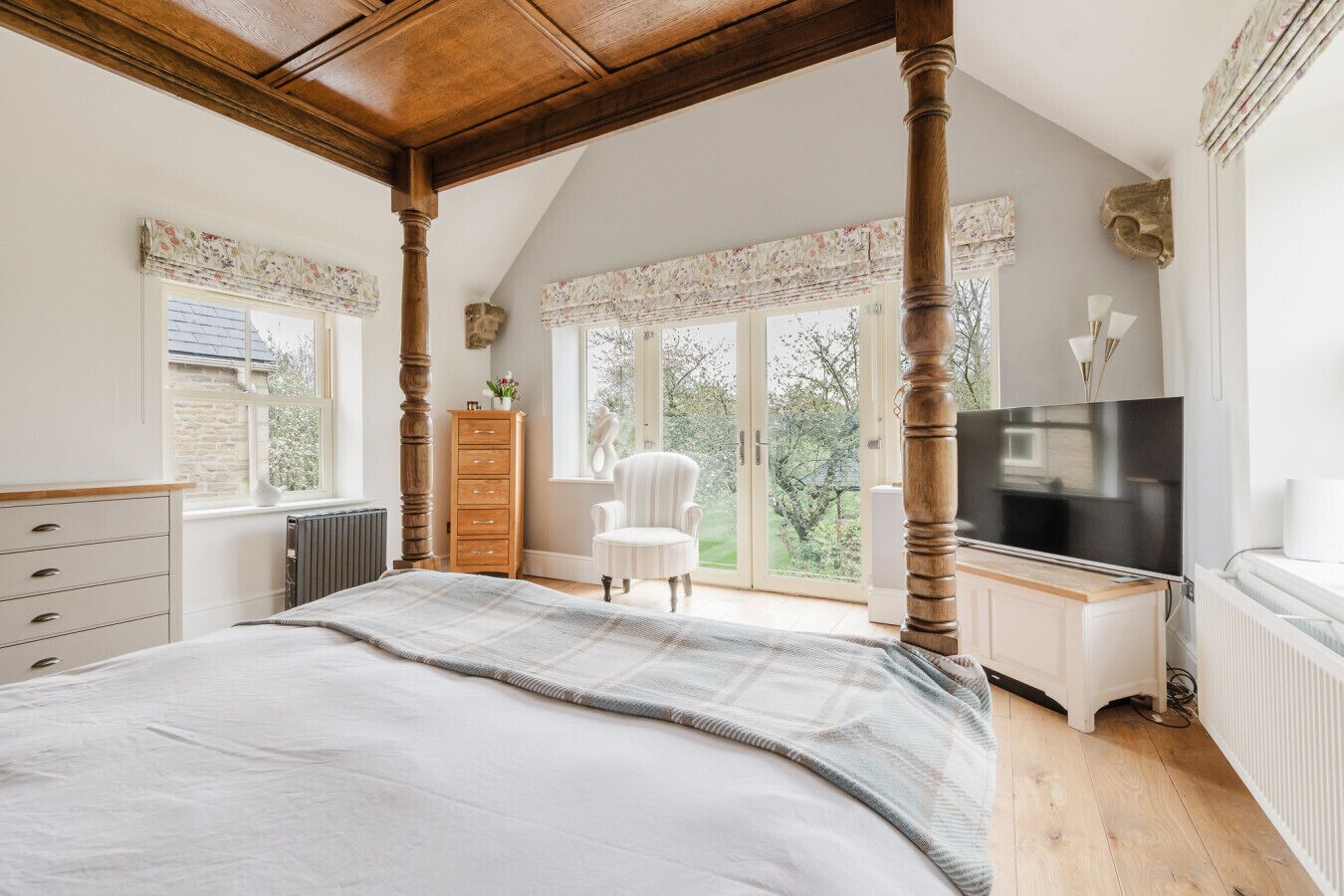 A bedroom with a large bed, a dresser, a chair, a TV, and a view of the outdoors.