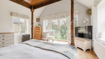 A bedroom with a large bed, a dresser, a chair, a TV, and a view of the outdoors.