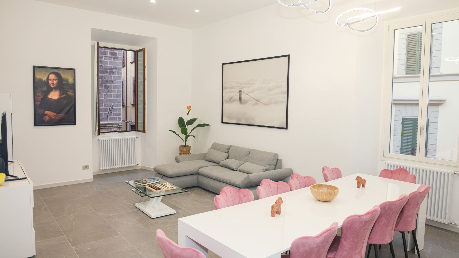 Ett modernt vardagsrum med en grå soffa, ett vitt matbord med rosa stolar och konstverk på väggarna.