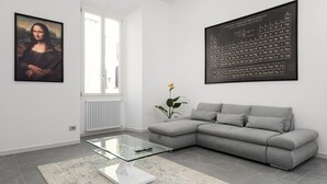 Una sala de estar moderna con un sofá gris, una mesa de centro de vidrio, un cuadro enmarcado y un gran cartel de tabla periódica en la pared.