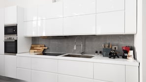 A modern kitchen with white cabinets, a double sink, a built-in oven, and a coffee machine.