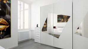 Une chambre avec une armoire blanche, un lit, un radiateur et une fenêtre.