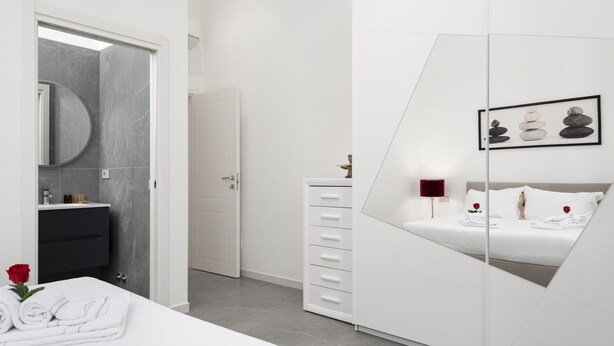 Una habitación de hotel moderna con una cama, un tocador con espejo, un aparador y una obra de arte enmarcada en la pared.