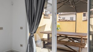Un balcón con una mesa y sillas de madera, una cortina gris y vistas a edificios al fondo.