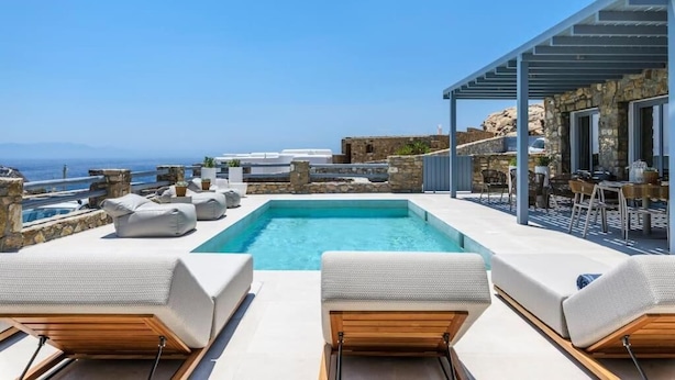 A rooftop pool with lounge chairs, a stone wall, and a view of the sea.